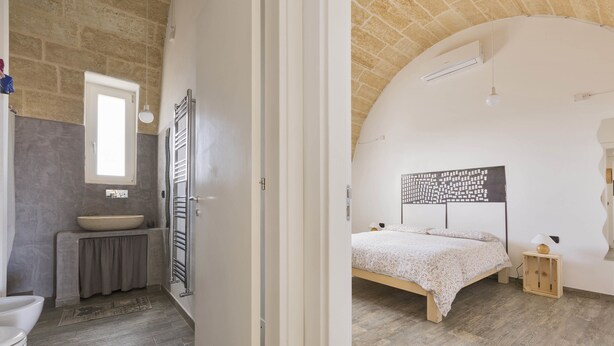 Um quarto com cama, mesa de cabeceira e luminária na parede.