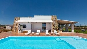 Uma casa moderna com piscina, paredes de pedra e um espaço de estar coberto.