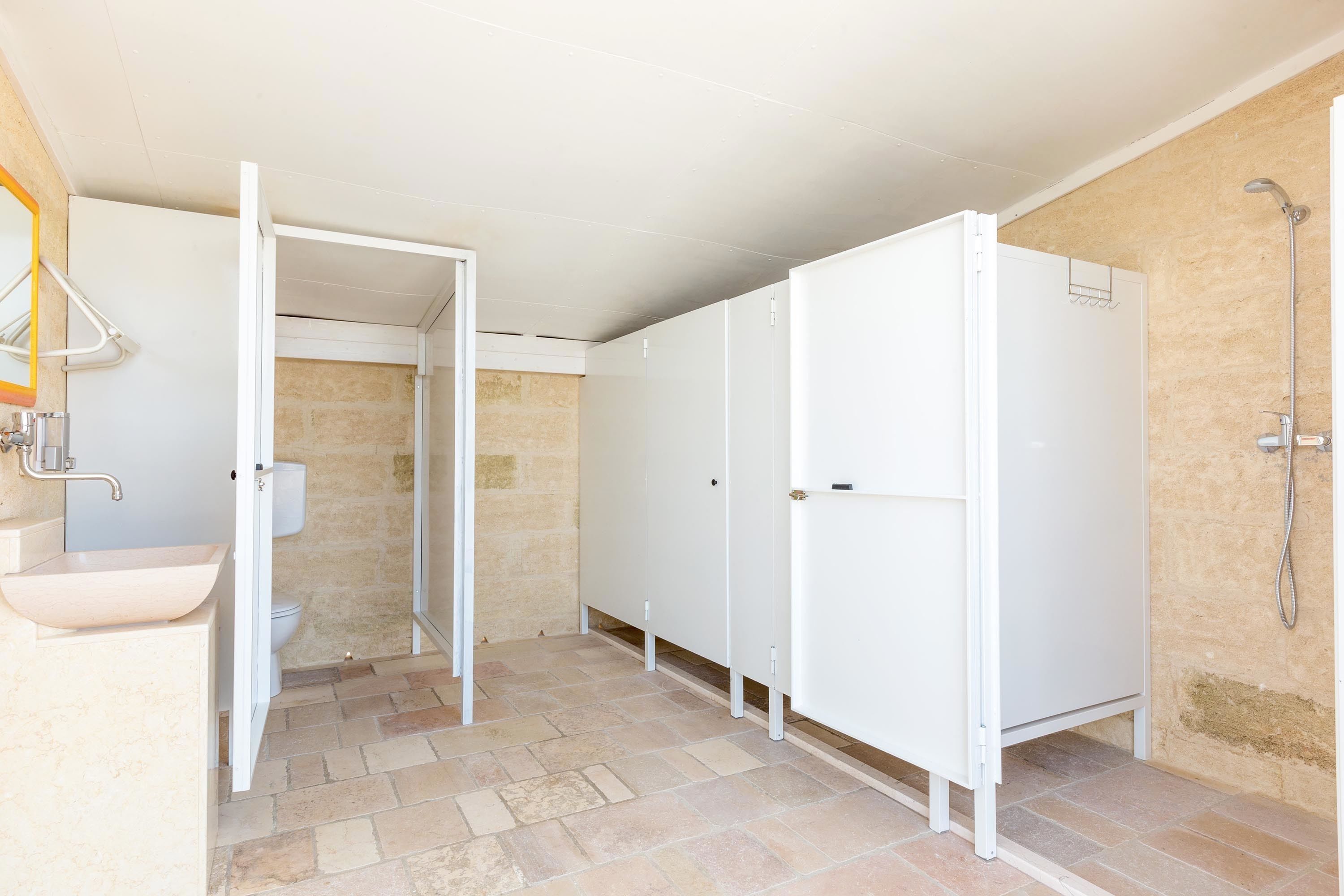 A bathroom with a white sink, toilet, and shower area. There are white cabinets and a tiled floor.