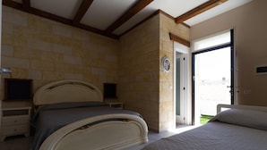 A bedroom with a bed, bedside tables, and a stone wall. - Villetta Giorgina (Porto Cesareo)