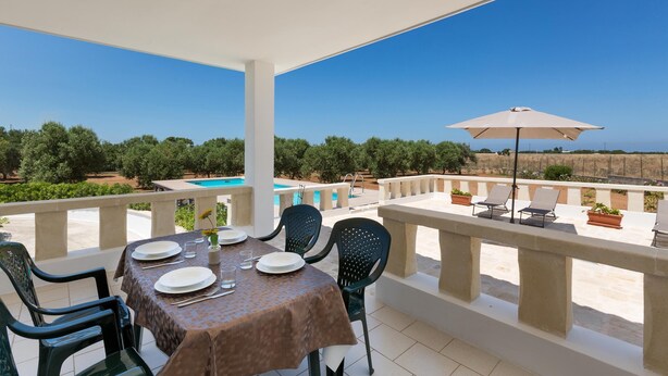 A terrace with a table set for dining, a pool, and a view of the landscape. - Villetta di Paulo (Carovigno)