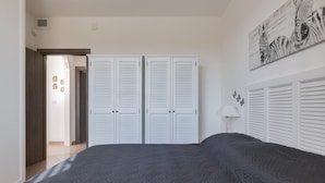 A bedroom with a large bed, white louvered closets, and a wall-mounted artwork. - Villetta di Paulo (Carovigno)