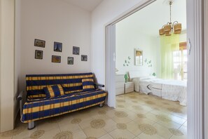 A room with a sofa, a bed, a small table, and a wall with pictures.