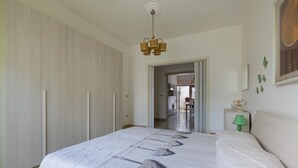 Une chambre avec un grand lit, une armoire, une lampe et une vue sur une autre pièce.