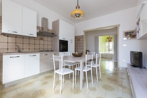 A modern kitchen with white cabinets, a dining table with chairs, a TV, and a yellow pendant light. - Villetta Lorena (Porto Cesareo)