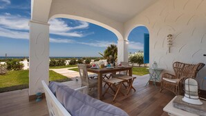 A covered outdoor seating area with a wooden table and chairs, a cushioned bench, and a view of the sea. - Villette Piramo (Ostuni)