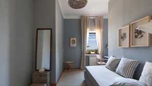 A bedroom with a large bed, a small table, a chair, a window with curtains, and artwork on the walls. - Villette Piramo (Ostuni)
