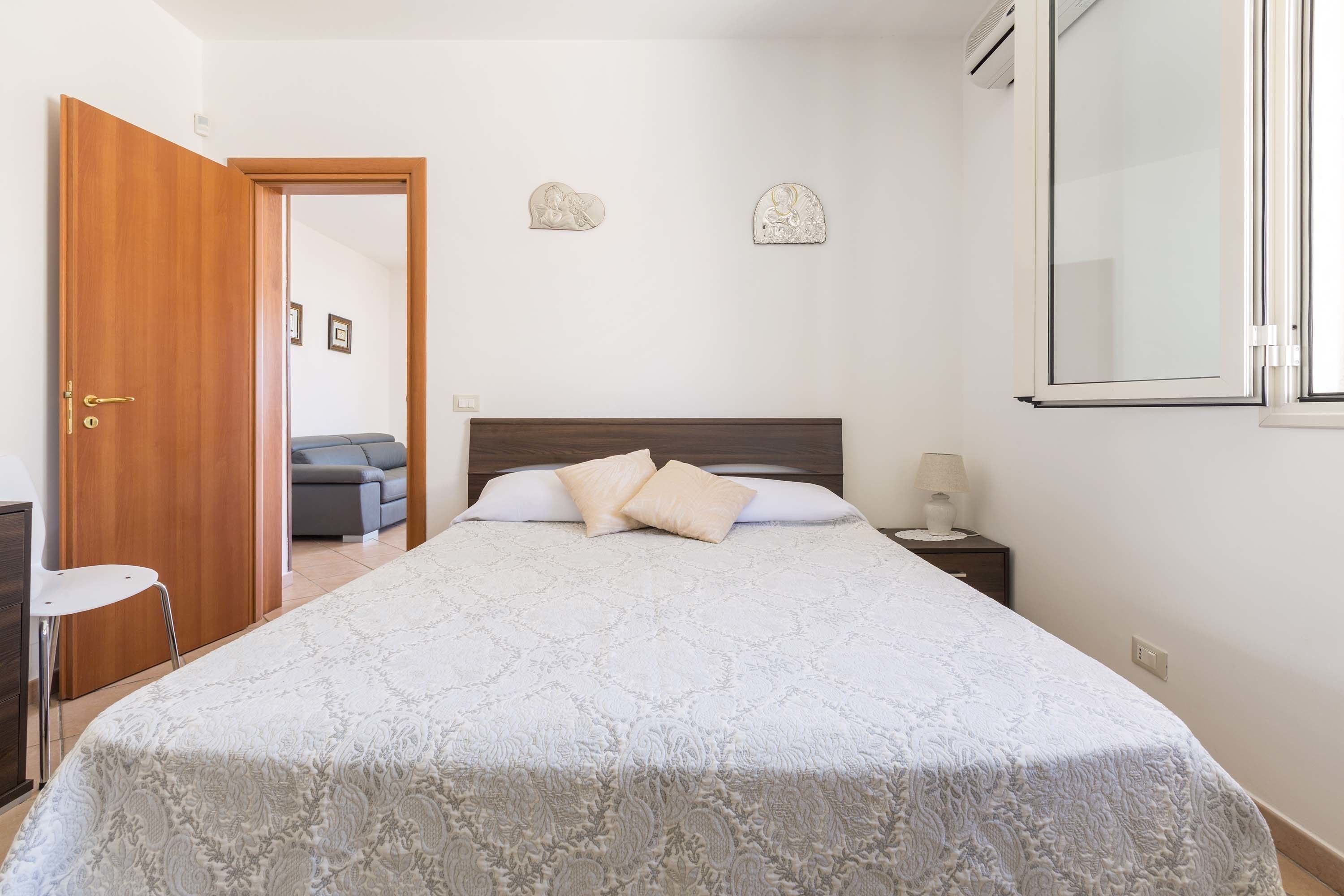 Une chambre à coucher comprenant un lit, une table de chevet, une lampe et une porte donnant sur une autre pièce.