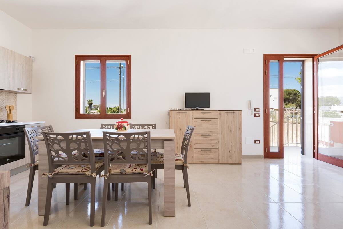 A modern kitchen with a dining area, wooden cabinets, and a TV on a cabinet.