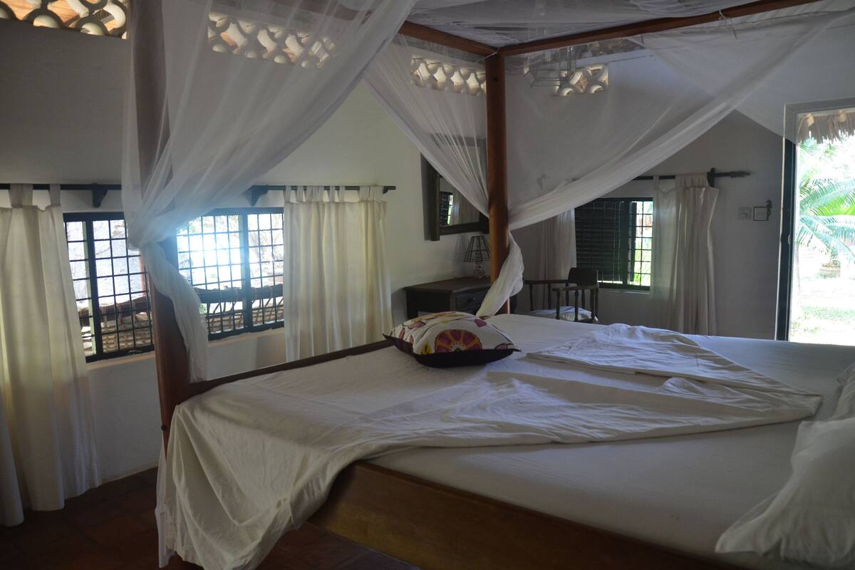 Quarto com cama grande, cortinas brancas e dossel.