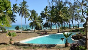 A pool surrounded by palm trees and a view of the ocean. - Diani house (Diani Beach)