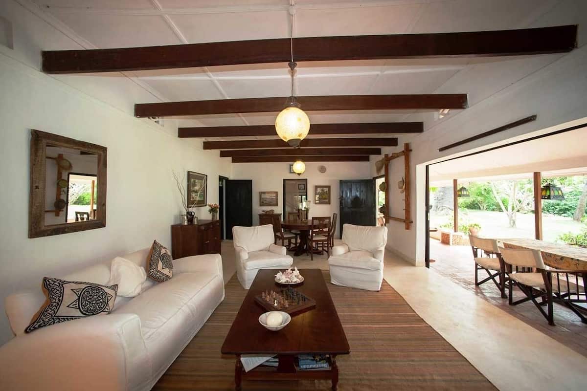 Uma sala de estar ampla com uma mesa de centro de madeira, sofás brancos e uma área de jantar com mesa e cadeiras de madeira.