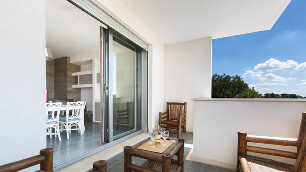 Een balkon met houten meubels, een tafel met glazen en een schuifpui naar een binnenruimte met een eethoek.
