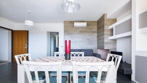Een eetgedeelte met een witte tafel en stoelen, een rode vaas en een moderne keuken op de achtergrond.