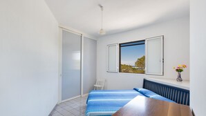 A bedroom with a bed, a wooden table, a radiator, a window with a view, and a white chair. -  909 Appartamento Porticciolo by Barbarhouse (Porto Cesareo)