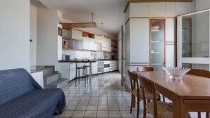 A modern kitchen with white cabinets, a wooden dining table, and a blue sofa. -  909 Appartamento Porticciolo by Barbarhouse (Porto Cesareo)
