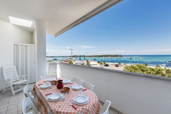 A balcony with a table set for dining, overlooking a marina with boats and a beach.