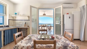 A dining area with a table set for four, a kitchen with a view of the sea, and a refrigerator. - Attico del Blu (Castrignano del Capo)