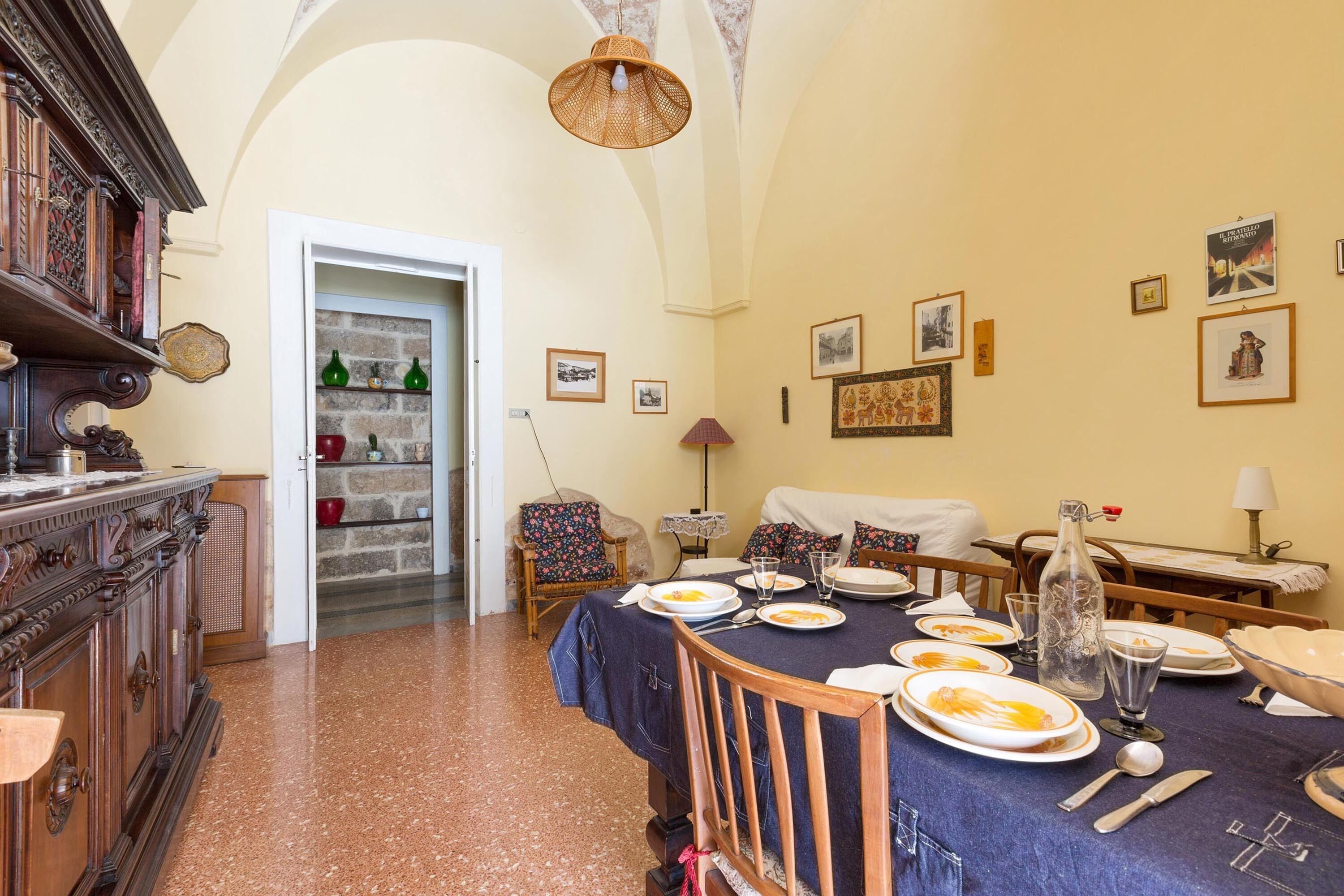 A dining area with a table set for four, a wooden cabinet, and a door leading to a kitchen.