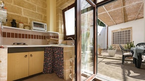 A kitchen with a stone wall, a window, and a view of an outdoor patio with a table and chairs. - Casa Messapica (Ugento)