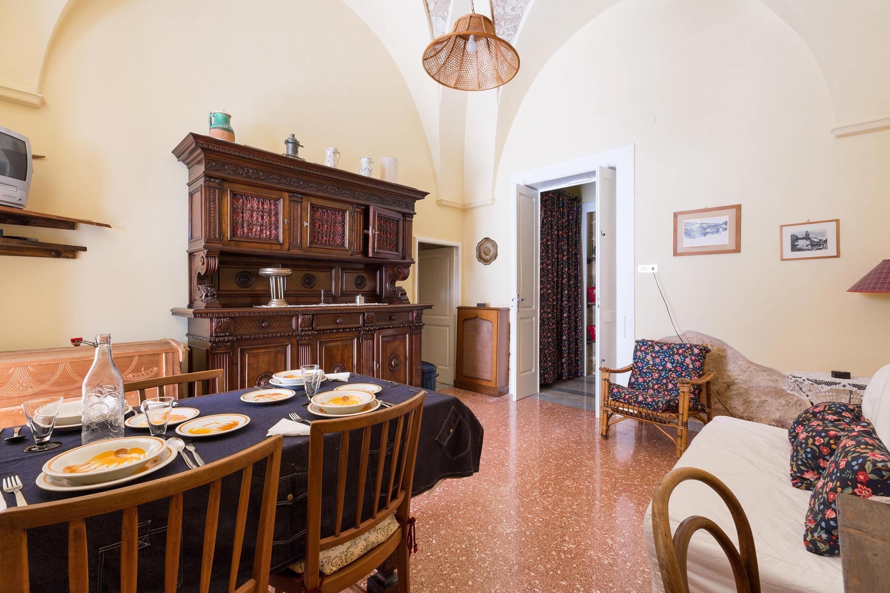 A dining area with a wooden table set for a meal, a wooden cabinet with decorative items, and a floral-patterned chair.