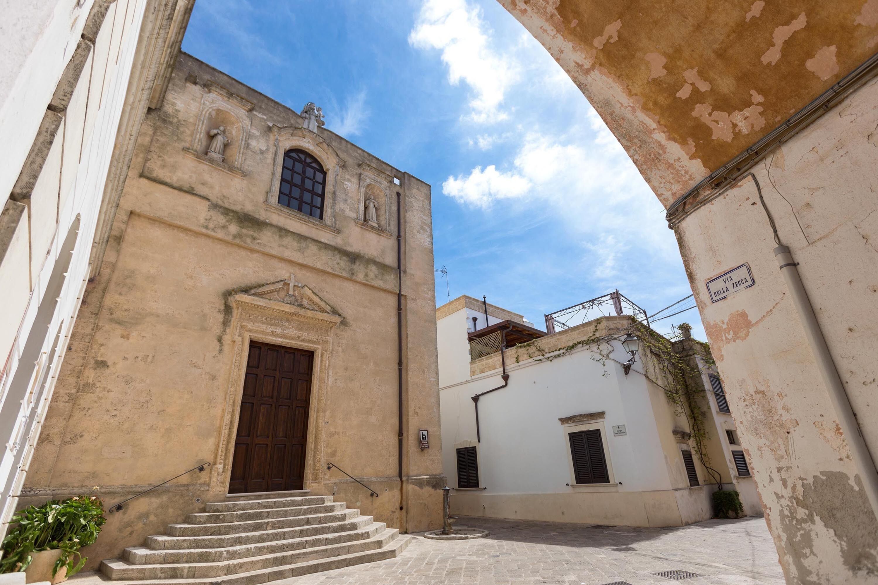 Una calle estrecha con un edificio que tiene una puerta de madera grande y escalones que la conducen.