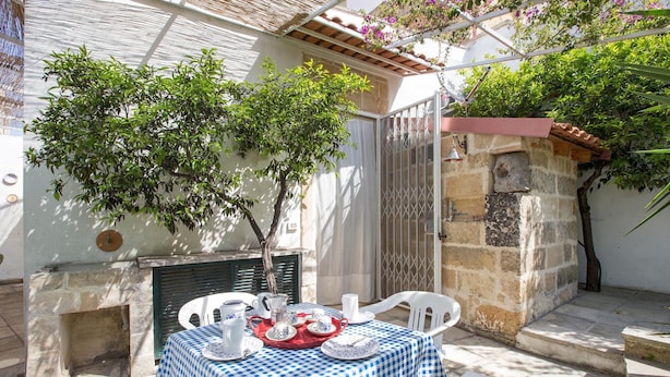 An outdoor patio with a checkered tablecloth, white chairs, and a stone wall. - Casa Messapica (Ugento)