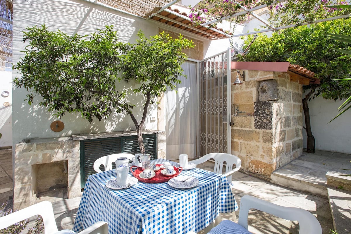 An outdoor patio with a checkered tablecloth, white chairs, and a stone wall.