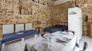 A stone-walled room with a bed, a bench, a table set for dining, and a refrigerator. - Casa Messapica (Ugento)