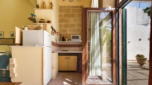 A compact kitchen with a refrigerator, a microwave, and a small oven. There is a wooden cabinet and a window with curtains. - Casa Messapica (Ugento)