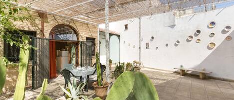 A courtyard with a covered seating area, potted cacti, and a wall with decorative plates.
