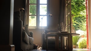 A cozy room with a large window, a chair, a table, and a lamp. - Les Chambres d'Andréa (Marseillan)