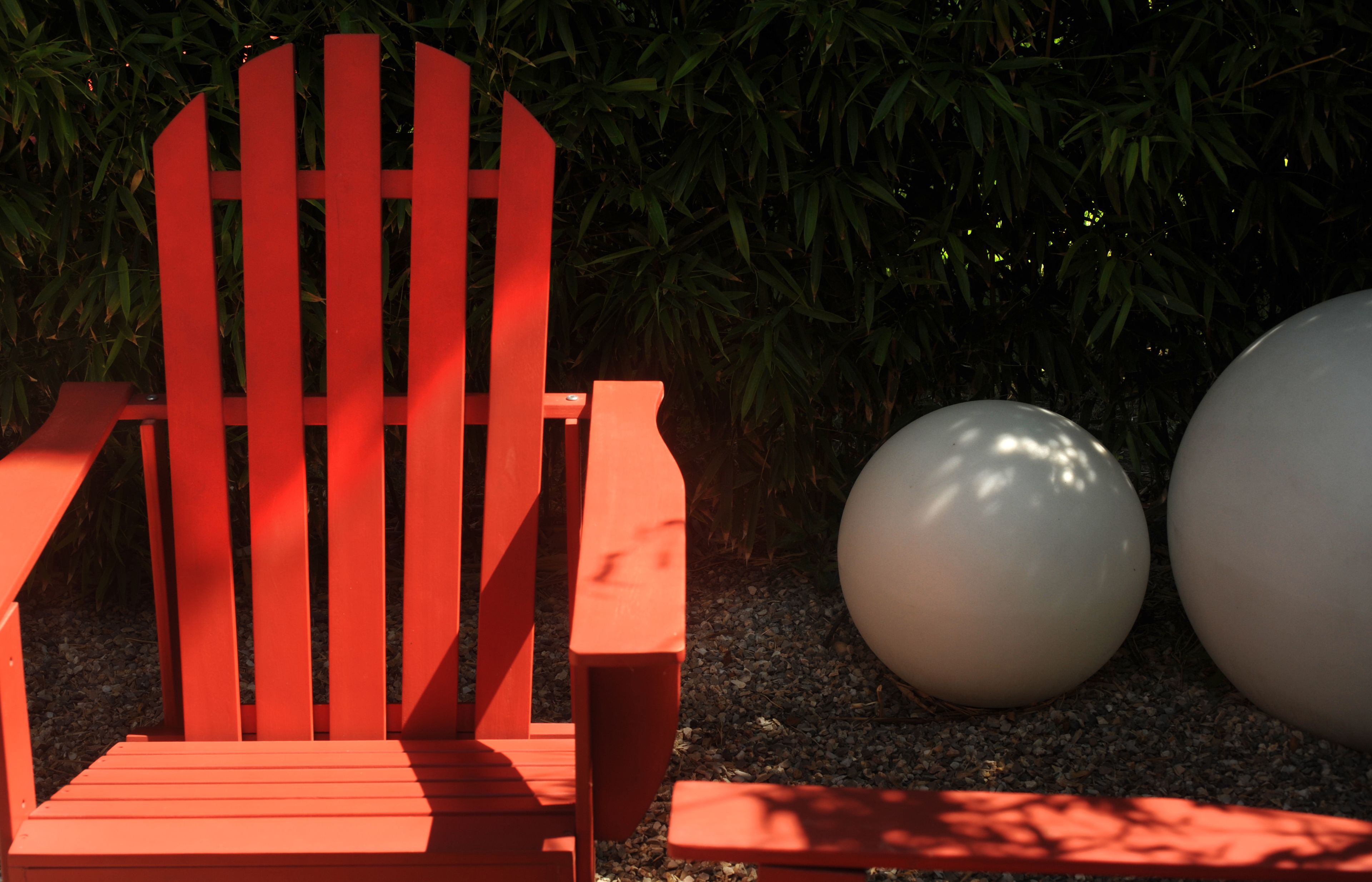 Una silla Adirondack roja en un jardín con dos esculturas esféricas blancas de gran tamaño.