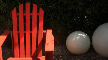 Una silla Adirondack roja en un jardín con dos esculturas esféricas blancas de gran tamaño.