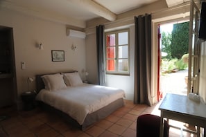A bedroom with a bed, bedside table, lamp, and a window with curtains. - Les Chambres d'Andréa (Marseillan)