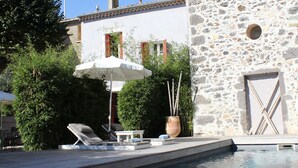 A stone building with a pool, a lounge chair, and a table with an umbrella. - Les Chambres d'Andréa (Marseillan)