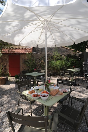 An outdoor dining area with tables and chairs under a large umbrella, surrounded by stone walls and greenery. - Les Chambres d'Andréa (Marseillan)