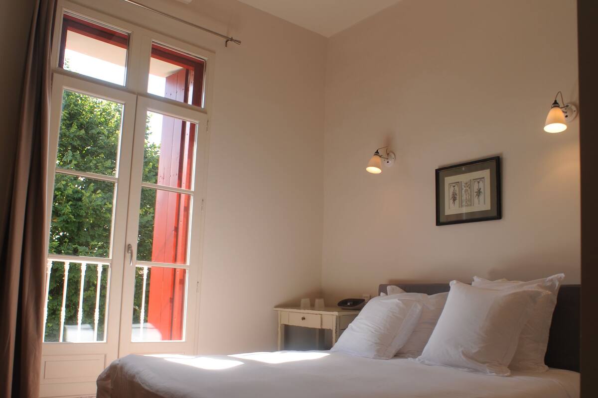 Un dormitorio con una cama, una mesita de noche, un cuadro enmarcado en la pared y una ventana con cortinas.