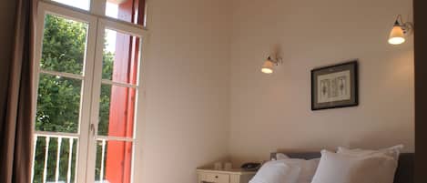 A bedroom with a bed, a nightstand, a framed picture on the wall, and a window with curtains.