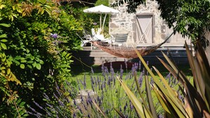 A hammock in a garden with lavender plants and a stone building in the background. - Les Chambres d'Andréa (Marseillan)