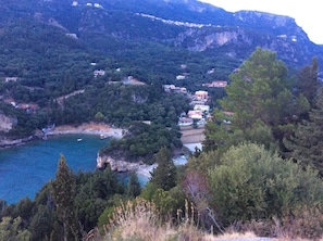 A coastal village with buildings nestled among green hills and a clear blue sea.
