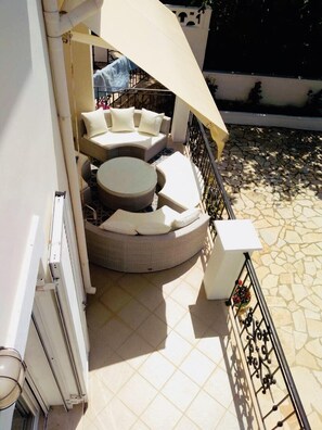 A sunlit outdoor seating area with a round table and cushioned chairs, a white awning, and a tiled patio floor.