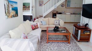 A living room with a sofa, coffee table, and a TV stand. There is a staircase leading to a kitchen. - Villa Ampelaki (30 meters to the beach) (Corfu)