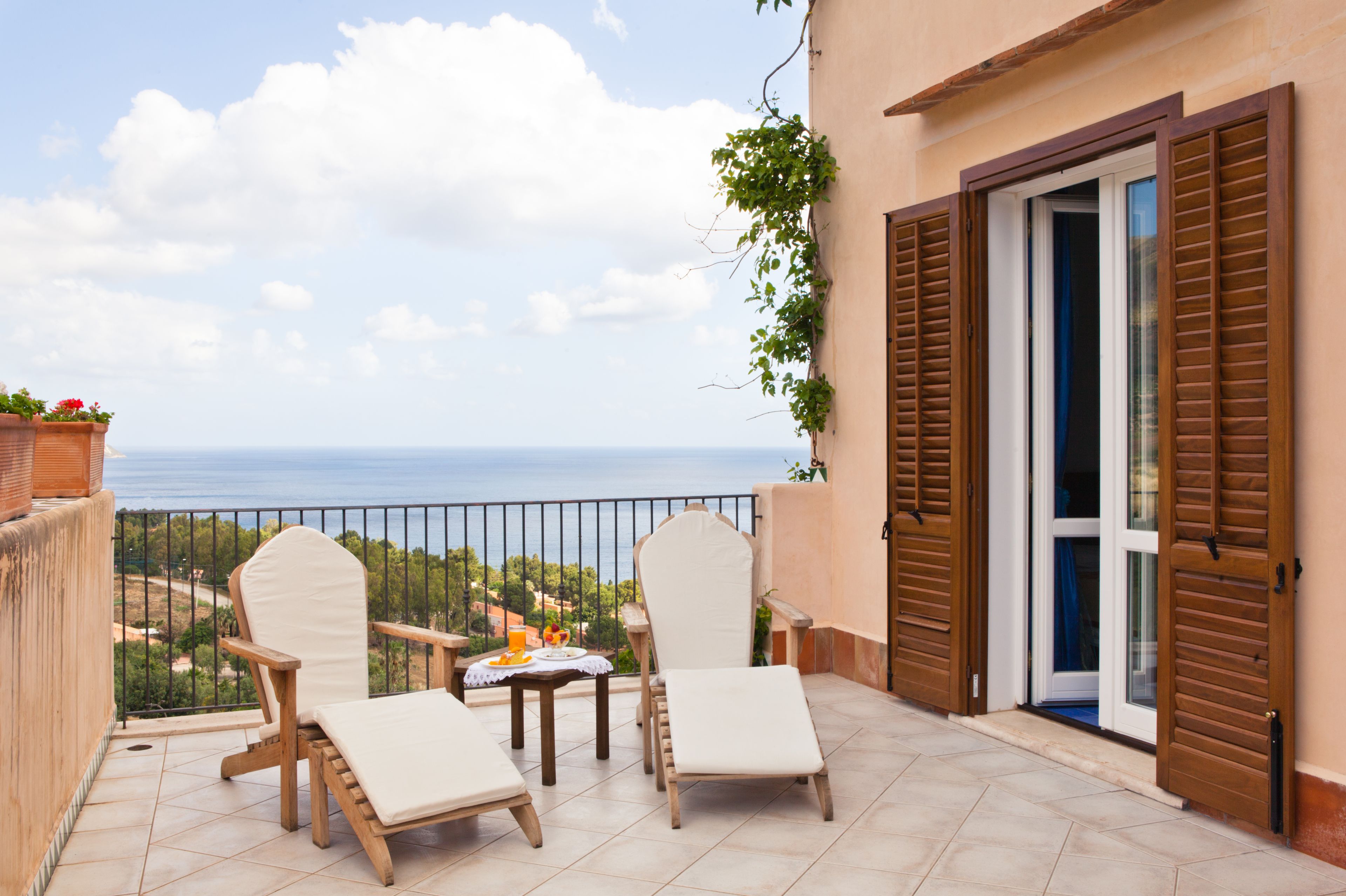 Ein Balkon mit zwei Stühlen, einem Tisch und einem Getränk, mit Blick aufs Meer.