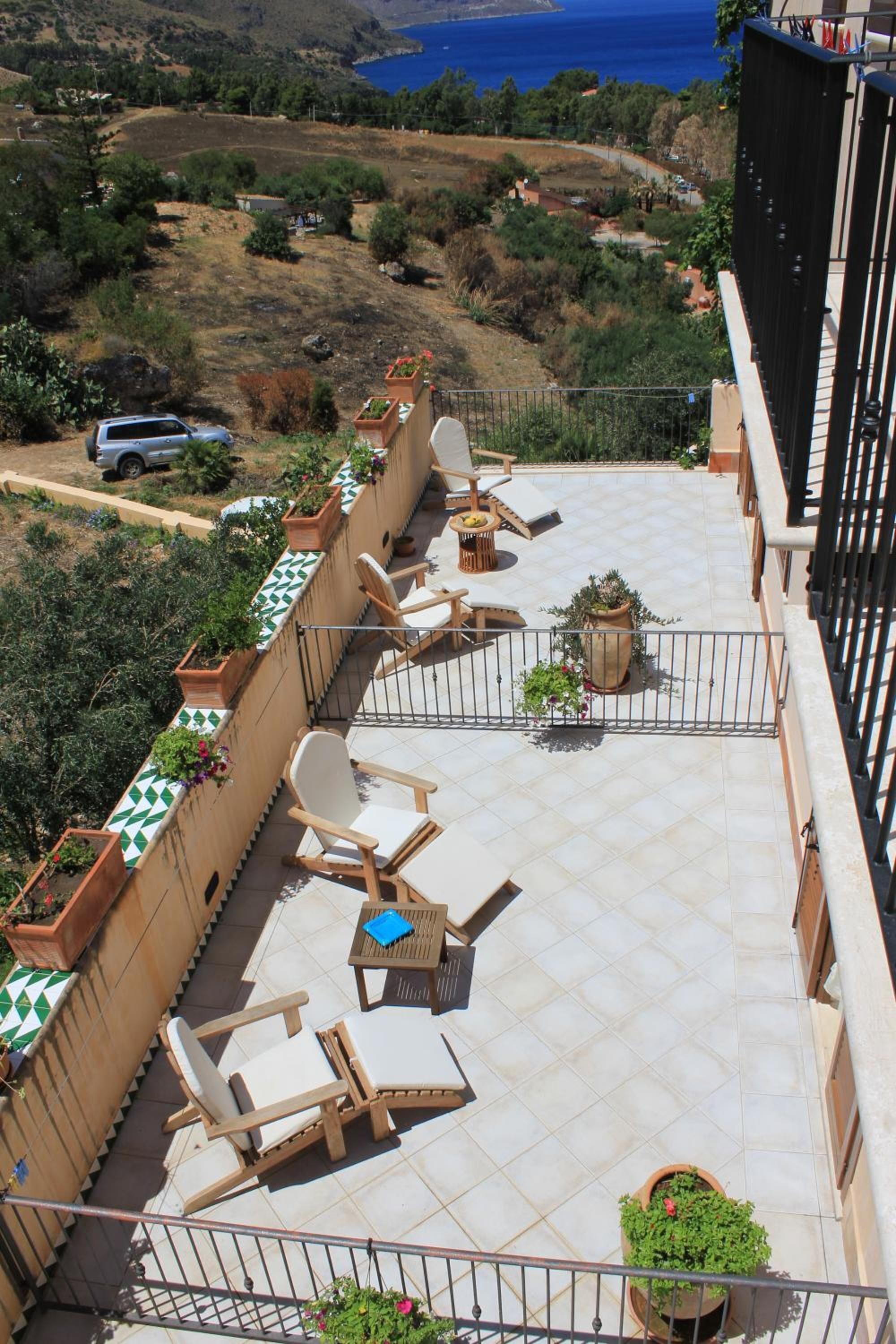 A rooftop terrace with outdoor furniture, potted plants, and a view of the sea.
