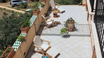 A rooftop terrace with outdoor furniture, potted plants, and a view of the sea.