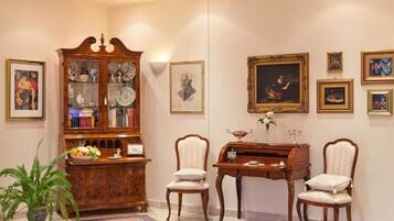 A room with a wooden cabinet, two chairs, a desk, and framed artwork on the wall.