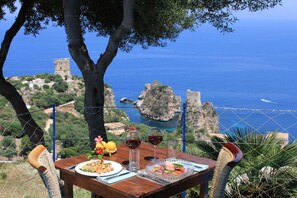 A table with a meal and drinks, overlooking a coastal landscape with a tower and rocky outcrops.