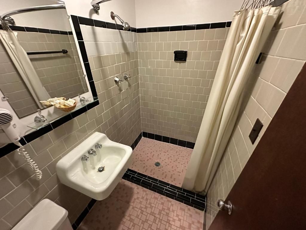 Un baño con lavamanos blanco, espejo, ducha con cortina y piso de baldosas.