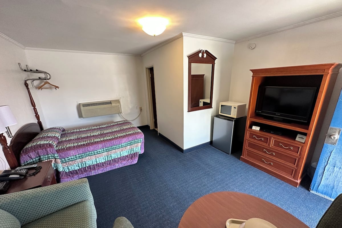 Une chambre d’hôtel comprenant un lit, un bureau avec une lampe, une télévision, un four à micro-ondes et une commode.